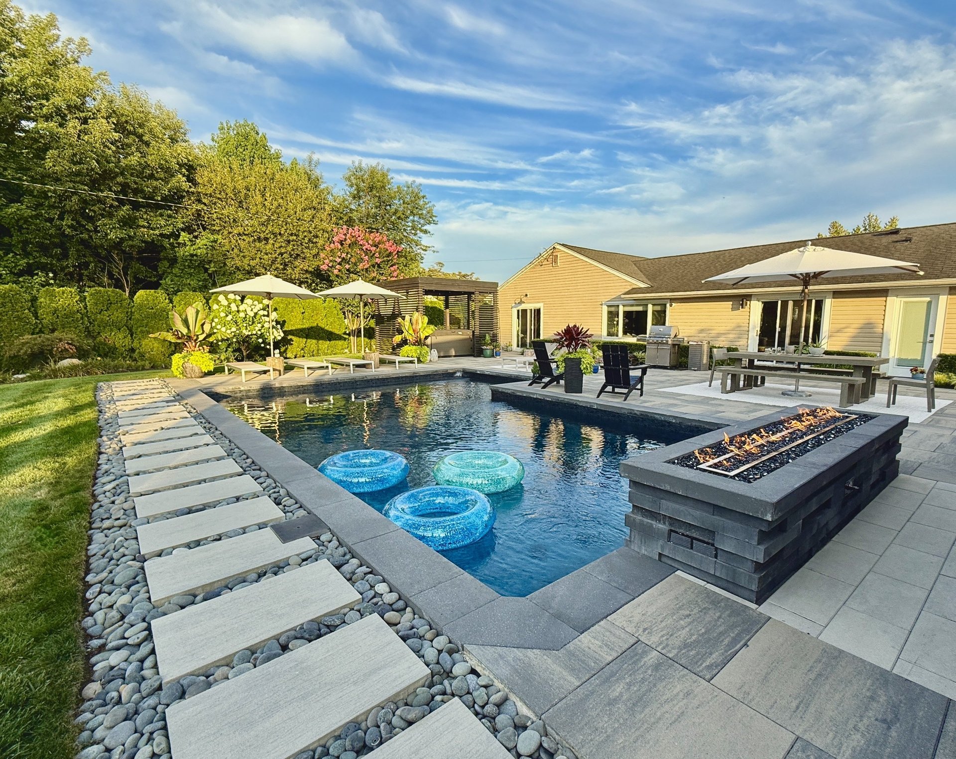 Clean sparkling residential swimming pool with pool deck lounge chairs and modern backyard landscaping