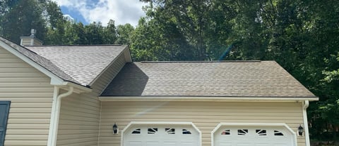 Exterior view of two-car garage with white doors attached to a cream-colored house with green trees in background