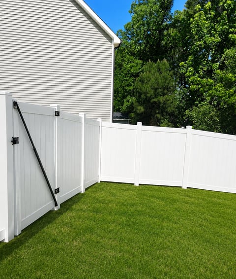 White vinyl fence with gate surrounding a green lawn