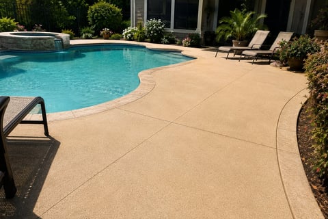 Luxury backyard with curved swimming pool, tan concrete deck, lounge chairs