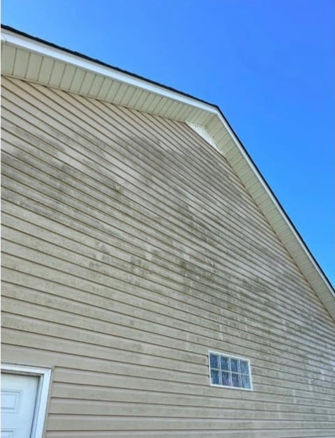 Gabled house exterior with beige horizontal siding, small window, and clear blue sky