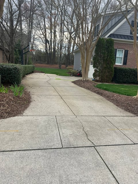 Concrete driveway and walkway leading to brick house with landscaped lawn and bare trees.