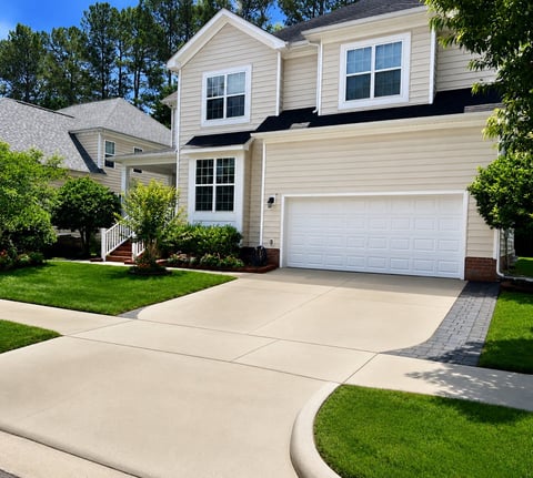 Two-story beige house with white garage door, curved driveway